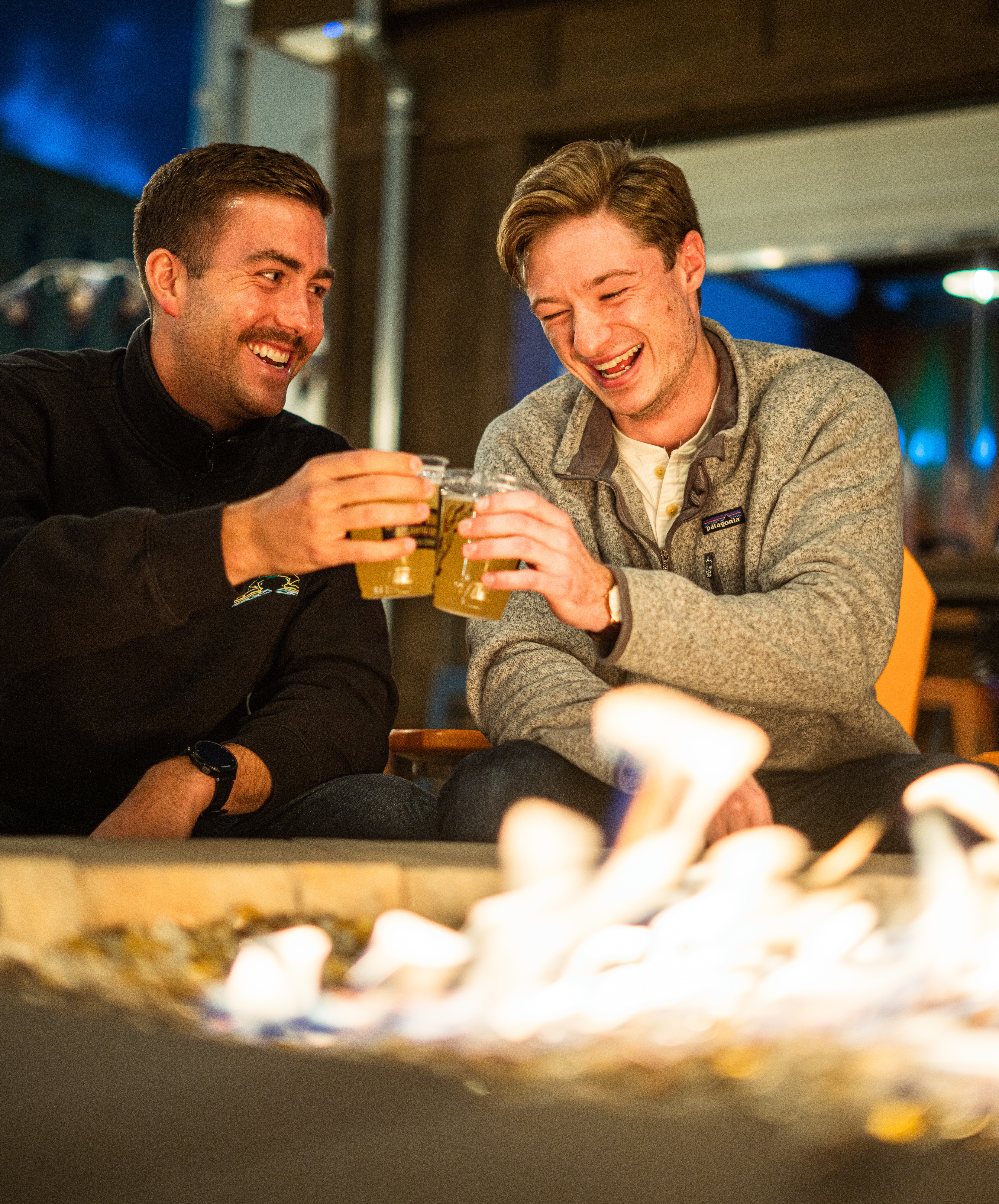 Deux hommes trinques autour d'un feu, avec un verre de bière.