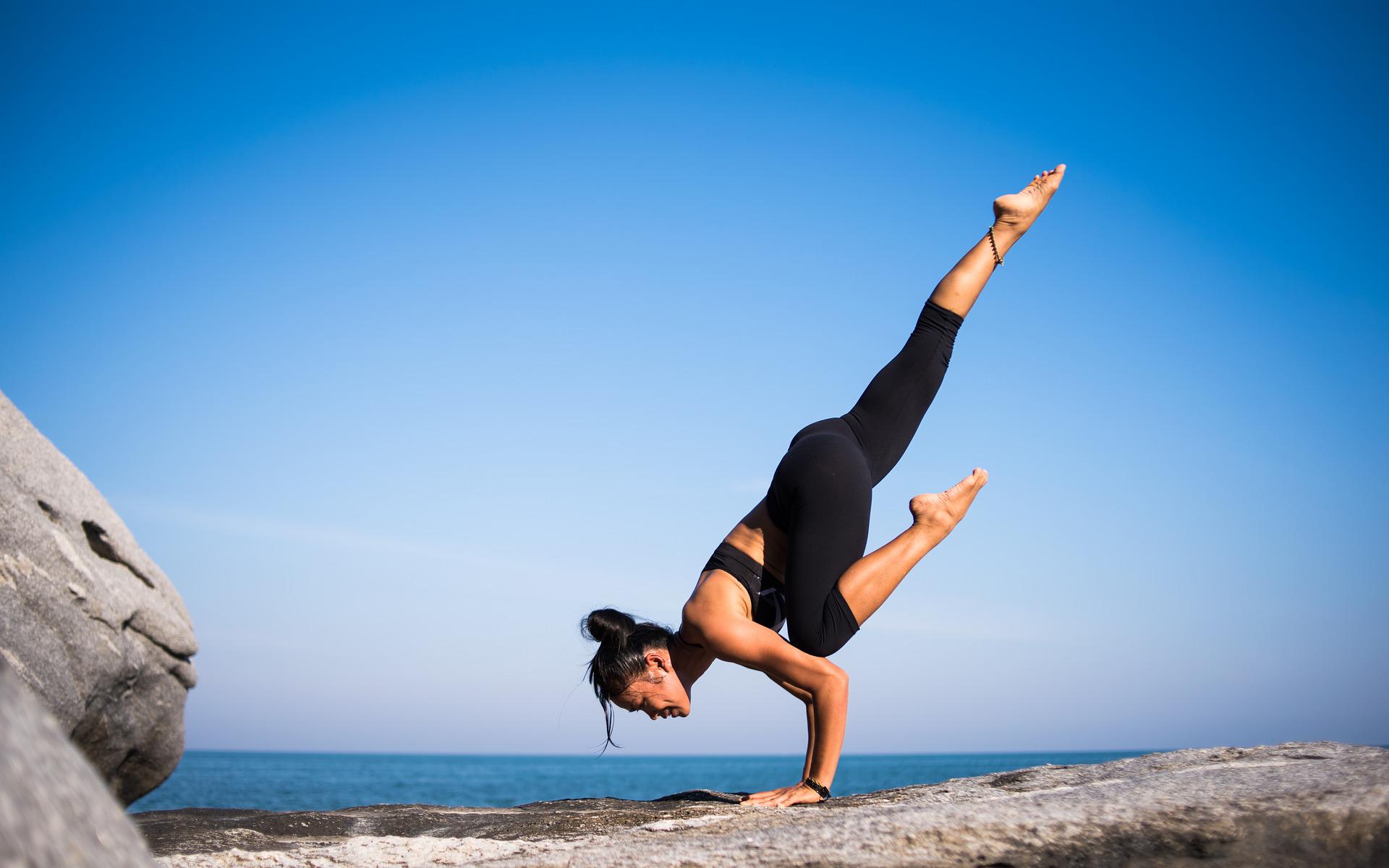 C'est une femme qui fait du yoga au bord de la plage. Actuellement, elle est en équilibre sur les bras dont elle est sur un rocher.